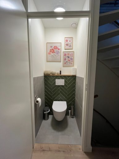 Kleine toiletruimte met groene tegels, toilet en kunst aan de muur.