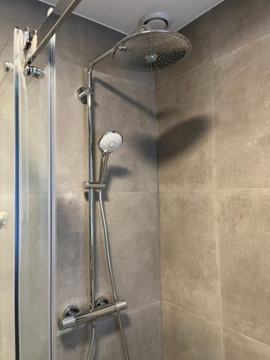 Moderne douche met verstelbare handdouche en regendouchekop in een betegelde badkamer.